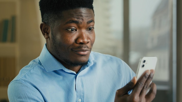 Sorprendido hombre de negocios africano joven empleado de oficina millennial feliz asombrado hombre ganador uso de móvil