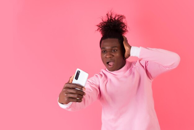 Foto sorprendido joven afro mirando el mensaje en su celular con una capucha rosa