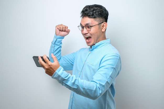 Sorprendido joven apuesto hombre asiático usando un teléfono inteligente para leer buenas noticias en línea