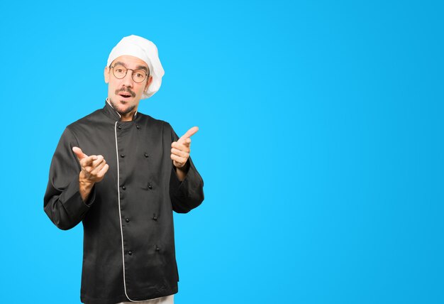 Sorprendido joven chef apuntando con su dedo
