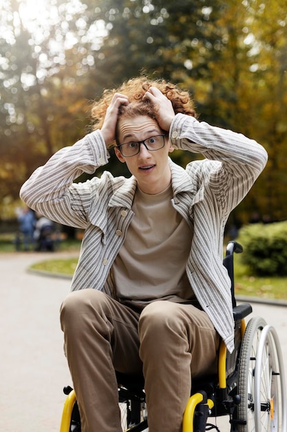 Foto sorprendido joven con gafas sostiene la cabeza con las manos un hombre se sienta en una silla de ruedas en la calle