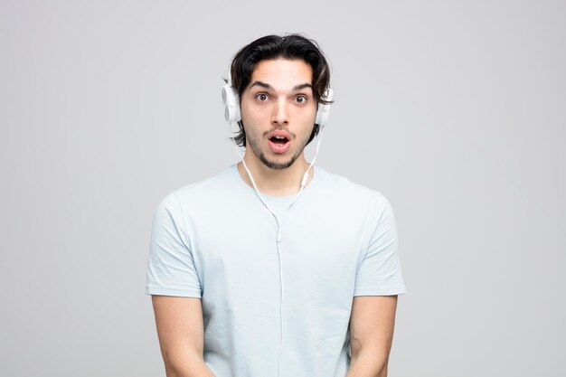 Sorprendido joven guapo con auriculares mirando a la cámara aislado sobre fondo blanco.