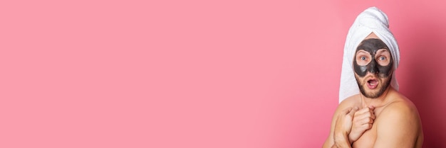 Foto sorprendido joven con máscara cosmética desnuda se esconde detrás de fondo rosa banner