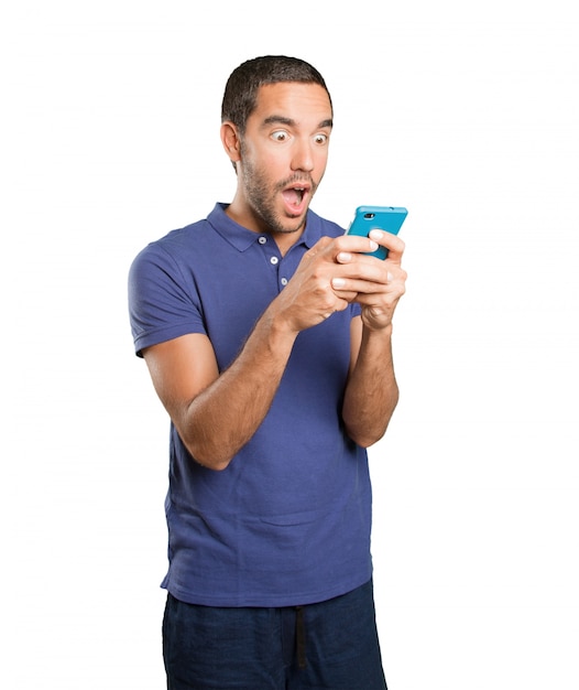 Foto sorprendido joven utilizando un teléfono móvil sobre fondo blanco