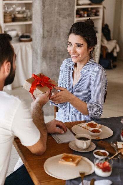 Sorprendido morena pareja hombre y mujer desayunando en el apartamento mientras está sentado a la mesa con el cuadro actual