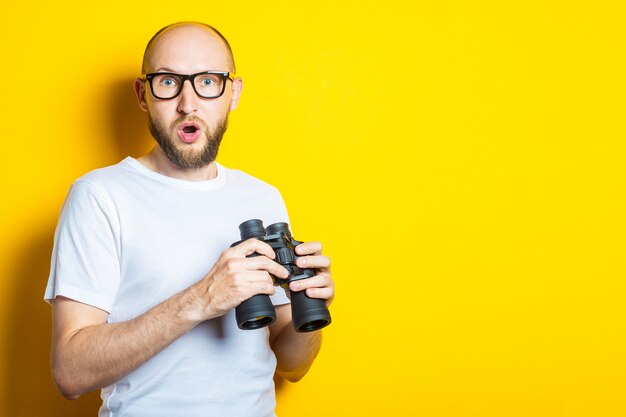 Sorprendido sorprendido joven barbudo con gafas sosteniendo binoculares