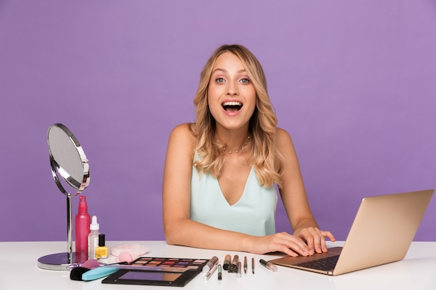 sorprendido sorprendido joven hermosa mujer con ordenador portátil y cosméticos con espejo.