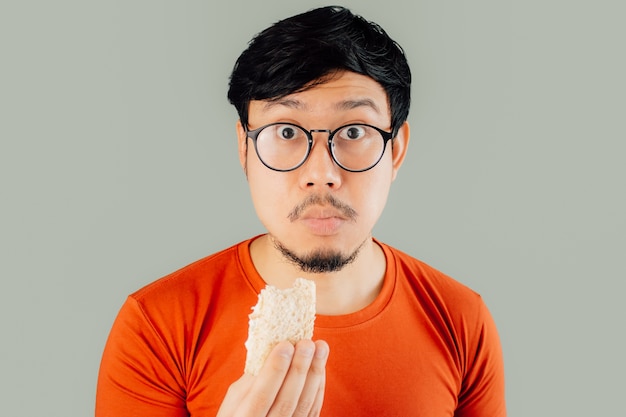 Sorprendido y sorprendido rostro de hombre asiático mientras come sándwich.