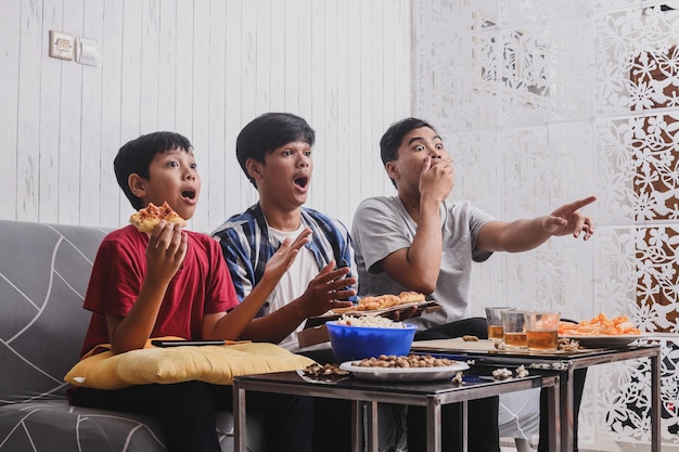 Sorprendidos hermanos asiáticos viendo una película de cine en la televisión sintiéndose sorprendidos y con una expresión de asombro