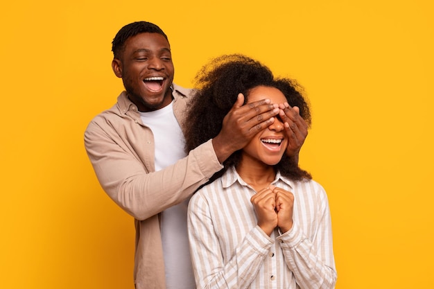 Sorpresa alegre hombre negro cubre los ojos de la mujer ambos riendo