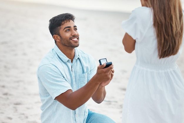 Sorpresa de propuesta y compromiso con anillo de bodas en la playa con un hombre indio de rodillas por compromiso de amor y matrimonio Guardar el regalo de fecha y joyas de diamantes para mujer para romance