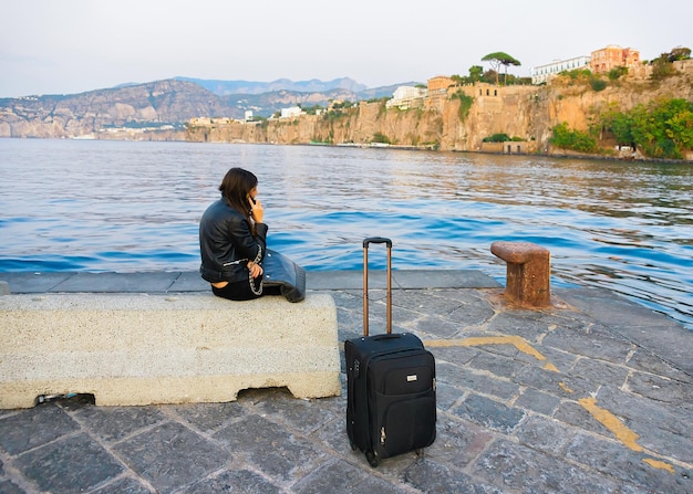 Foto sorrento, italien - 2. oktober 2017: frau im gespräch per handy mit ihrer gepäcktasche im hafen von marina grande in sorrento, tyrrhenisches meer, amalfiküste, italien