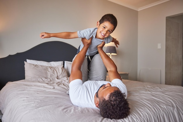 Sorria amor e feliz pai e filho tempo em família brincando na cama do quarto levantando-o como avião ou super-herói Pai amoroso ou pai solteiro se unindo com criança alegre pela manhã em casa