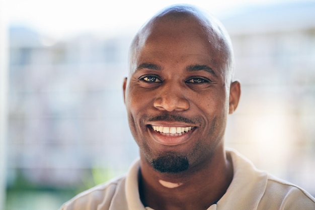 Sorria feliz e retrato de um empresário no escritório com confiança e atitude positiva Jovem carreira e rosto de designer masculino africano profissional em pé em um local de trabalho moderno