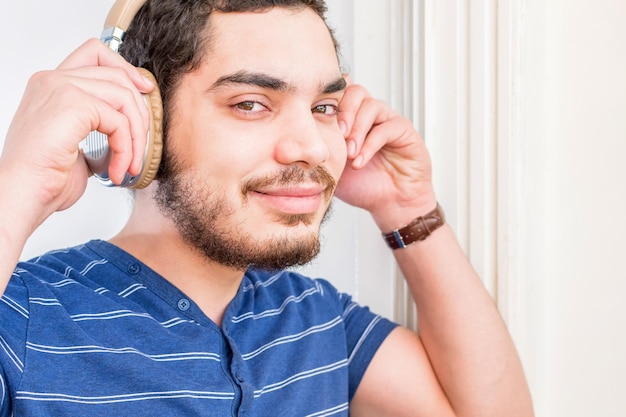 Foto sorria jovem com barba ouvindo música com fones de ouvido sem fio olhando para a câmera