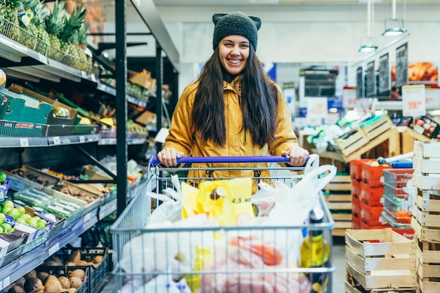 Sorria mulher com carrinho nas compras de supermercado