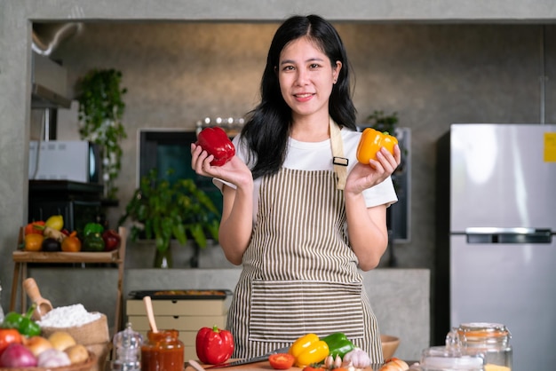 Foto sorria, uma chef asiática feliz segura vegetais nutritivos frescos para cozinhar uma refeição saudável na cozinha