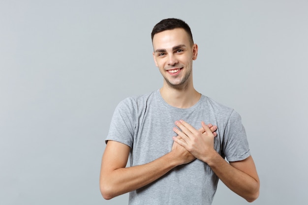 Sorridente agradável jovem em roupas casuais, com as palmas das mãos cruzadas no peito do coração