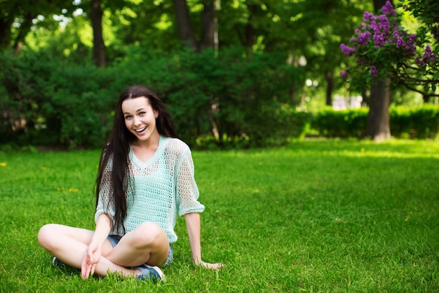 Sorridente bela jovem sentada na grama, contra o verde do parque primavera.