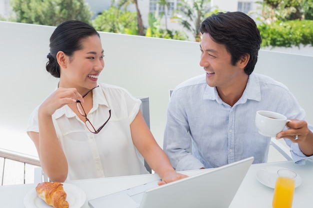 Sorridente casal com café da manhã juntos usando laptop