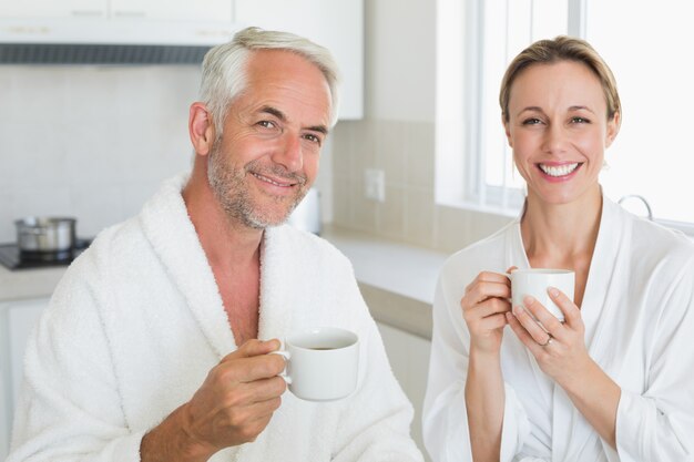 Sorridente casal com café no café da manhã em roupões de banho