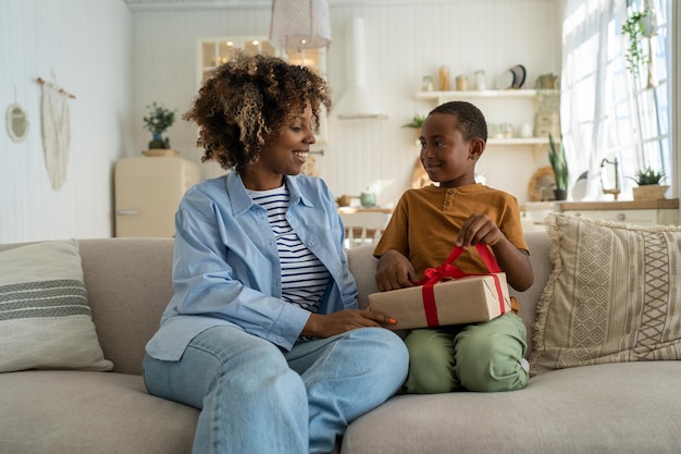 Sorridente e animada mãe afro-americana recebendo presente de aniversário do filho em casa
