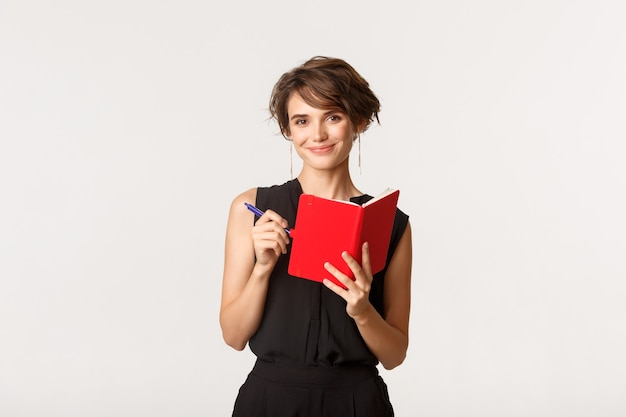 Sorridente e atraente empresária escrevendo sua agenda no planejador