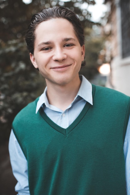 Foto sorridente e bonito estudante adolescente de 1718 anos usa colete de malha e camisa ao ar livre