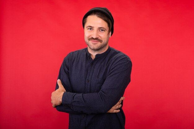 Sorridente e bonito hipster com barba por fazer com boné de malha posando de braços cruzados