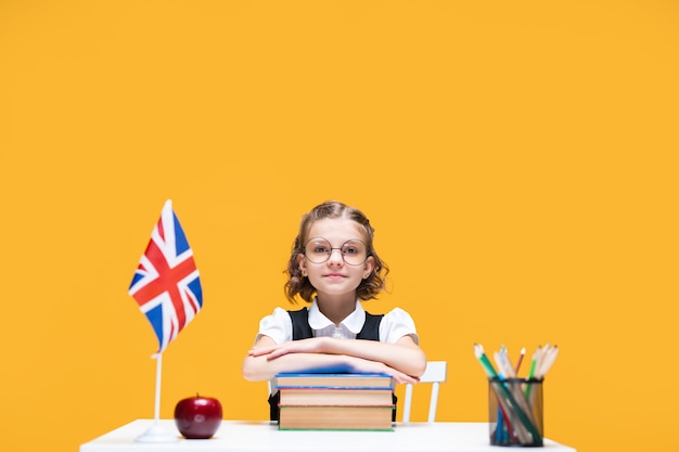 Sorridente e feliz aluna caucasiana sentada na mesa com livros, aula de inglês, bandeira da grã-bretanha