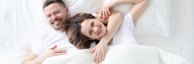 Sorridente e feliz, homem e mulher deitam-se abraçados na cama, segredos do conceito de vida familiar feliz