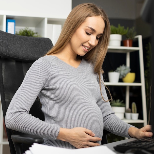 Sorridente empresária grávida em sua mesa no escritório
