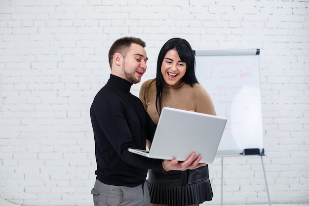 Sorridente empresário e gerente de mulher estão de pé com o laptop e olhando para a tela. Fique sobre um fundo branco.