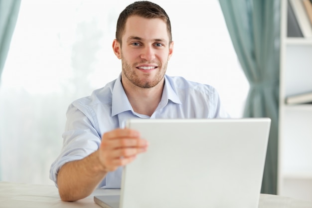 Sorridente empresário sentado atrás de uma mesa em seu laptop