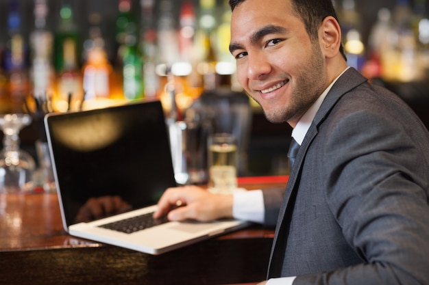 Sorridente empresário trabalhando em seu laptop enquanto toma uma bebida