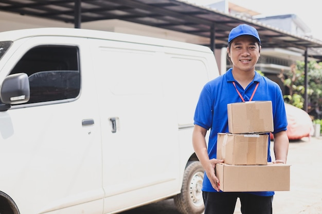 Sorridente entregador de uniforme azul segura pilha de caixas fora da van de transporte