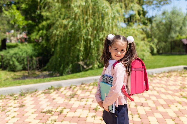 Sorridente garotinha bonitinha de uniforme com mochila escolar de volta à escola 1 de setembro