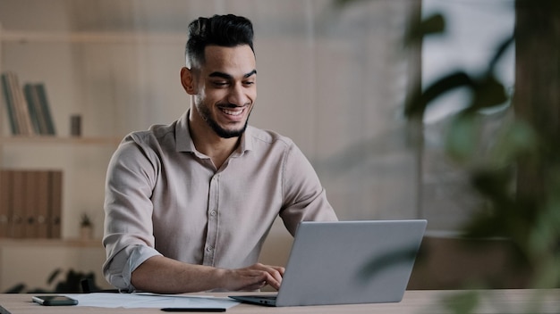 Sorridente homem árabe feliz trabalhador empresário terminou a tarefa trabalho de computador relaxe sente-se na mesa do local de trabalho