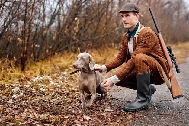 Sorridente homem confiante europeu de terno marrom na moda com cão raça weimaraner caminha no campo...