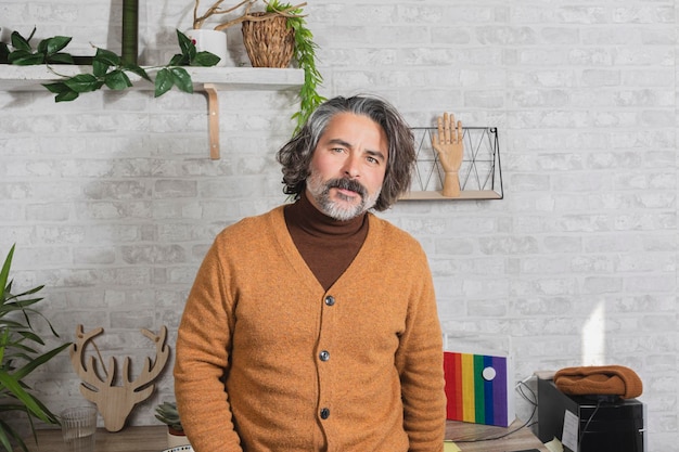 Sorridente homem hipster freelancer em pé na mesa com o computador olhando para a câmera Homem bonito posando para uma foto em seu estúdio