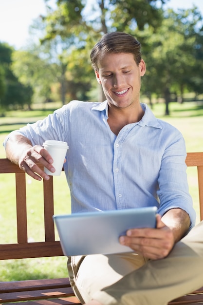 Sorridente, homem, sentando, parque, banco, usando, comprimido, bebendo, café