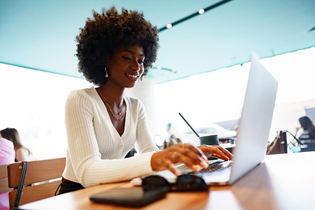 Sorridente jovem africana sentada com laptop no café