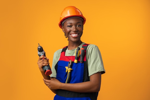 Sorridente jovem afro-americana no capacete segurando a ferramenta chave de fenda no estúdio