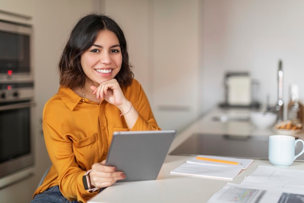 Sorridente jovem árabe freelancer usando tablet digital enquanto está sentado na cozinha