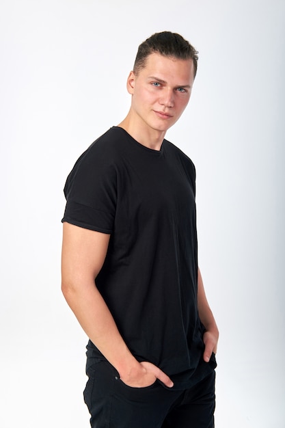 Foto sorridente jovem atraente vestindo uma camiseta de manga curta de algodão preto e calça jeans preta, posando no estúdio. estúdio, tiro em um fundo branco.