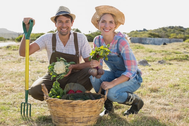 Sorridente jovem casal com legumes no campo