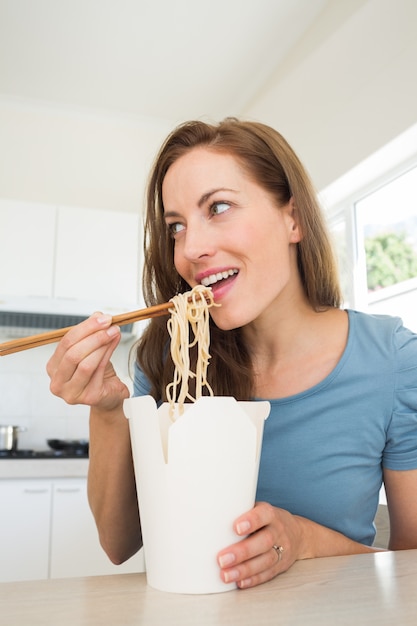 Sorridente jovem comendo macarrão na cozinha