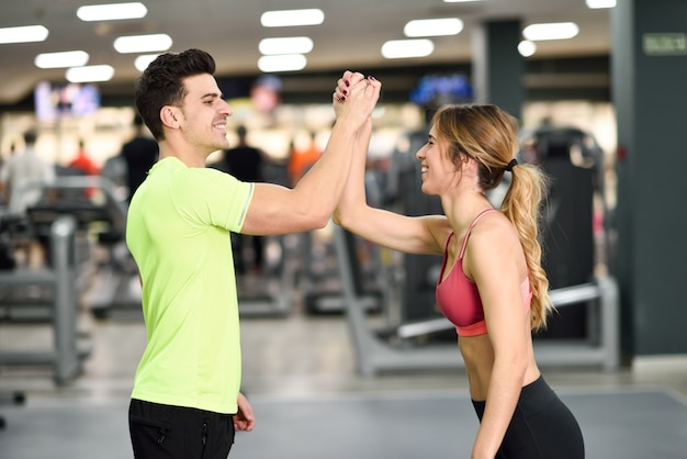 Sorridente jovem e mulher fazendo alta cinco na academia