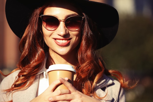 Sorridente jovem elegante tomando café enquanto caminhava em uma rua da cidade