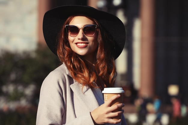 Sorridente jovem elegante tomando café enquanto caminhava em uma rua da cidade